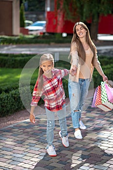 Smiling girl tugging her mom with shopping bags outside