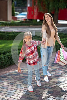 Smiling girl tugging her mom with shopping bags outside photo