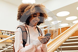 Smiling girl typing on smartphone while leaning rail in a library