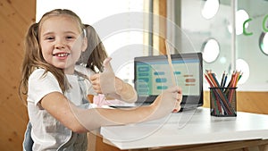 Smiling girl using laptop while look and show thumb up to camera. Erudition.