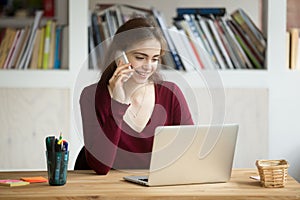 Smiling girl using laptop making answering call sitting at desk