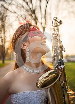 A smiling girl in a wedding dress with a red lace mask, and saxophone