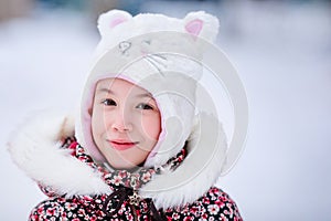 Smiling girl with white fur hat like a cat. Winter snowy background