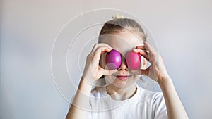 Smiling girl in a white t-shirt closes her eyes with multi-colored Easter painted eggs.