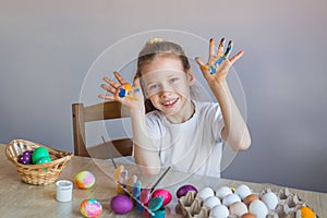 A smiling girl in a white T-shirt shows her palms covered in paint stained with eggs. Easter. Spring. Painted eggs.