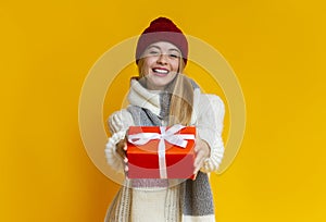 Smiling girl in winter clothes giving xmas gift