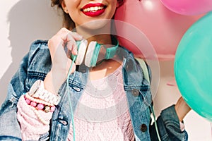 Smiling girl with wristwatch and cute handmade accessories holding new big turquoise headphones. Charming young woman