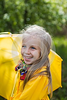 Smiling girl in a yellow dress with an umbrella on a rainy spring sunny day