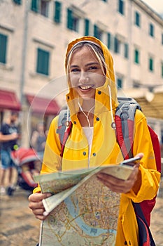 Smiling   girl with a yellow raincoat and map on the street while enjoying a walk through the city on a rainy day