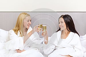 Smiling girlfriends with champagne glasses in bed