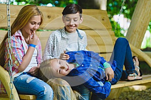 Smiling girls and boy having fun at playground. Children playing outdoors in summer. Teenagers on a swing.