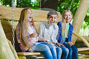 Smiling girls and boy having fun at playground. Children playing outdoors in summer. Teenagers on a swing.