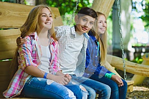 Smiling girls and boy having fun at playground. Children playing outdoors in summer. Teenagers on a swing.