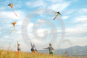 Smiling girls and brother boy with flying colorful kites - popular outdoor toy on the high grass mountain meadow. Happy childhood photo