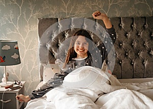 Smiling girls in grey pyjamas sitting,  yawning and stretching on the bed in the morning