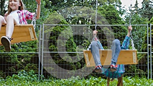 Smiling girls having fun at playground. Children playing outdoors in summer. Teenagers riding on a swing outside