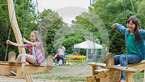 Smiling girls having fun at playground. Children playing outdoors in summer. Teenagers riding on a swing outside