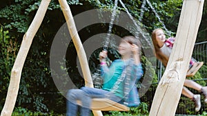Smiling girls having fun at playground. Children playing outdoors in summer. Teenagers riding on a swing outside
