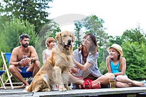 Smiling girls stroking Golden retriever while sitting with family on pier