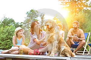 Smiling girls stroking Golden retriever while sitting with family on pier