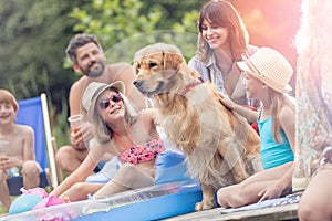 Smiling girls stroking Golden retriever while sitting with family on pier