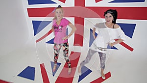 Smiling girls in t-shirts look at camera and dance in white studio with UK flag