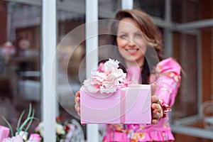 Smiling glorious brown-haired woman showing holiday present wrapped in pink box on birthday, Valentines Day or 8 march