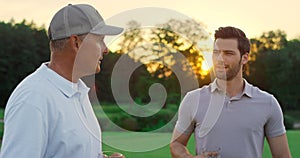 Smiling golf group talking on sunset fairway. Two players enjoy drink on course.