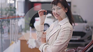 Smiling gorgeous Caucasian female buyer bragging car key standing in dealership looking at camera. Portrait of happy