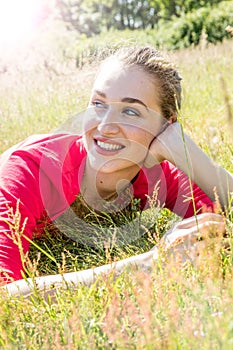 Smiling gorgeous young woman relaxing in the grass, breathing wellbeing