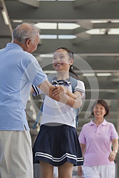 Smiling granddaughter embracing her grandfather with grandmother in background