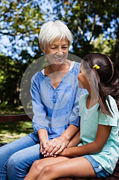 Smiling granddaughter and grandmother holding hands while sitting on bench