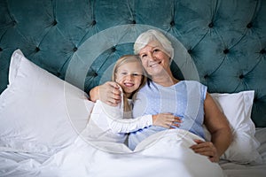 Smiling granddaughter and grandmother sitting together on bed