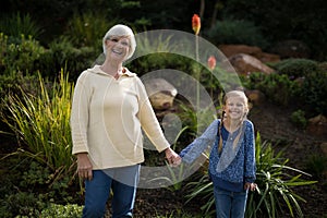 Smiling granddaughter and grandmother standing in garden
