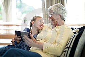 Smiling granddaughter and grandmother using digital tablet on sofa