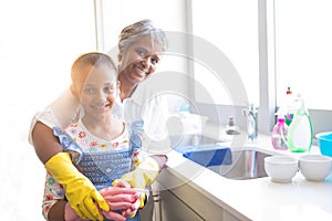 Smiling granddaughter and grandmother wearing kitchen gloves in kitchen