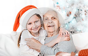 smiling granddaughter in santa hat hugging with grandma