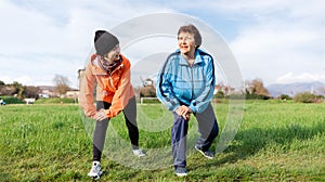 Smiling grandmother and granddaughter doing sports together in the park. Old and young women in sports clothes do a warm