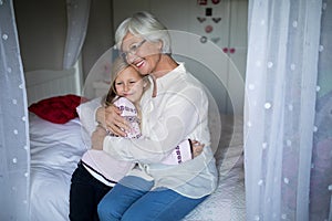 Smiling grandmother and granddaughter embracing each other on bed