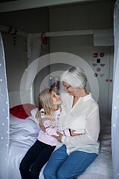 Smiling grandmother and granddaughter embracing each other on bed