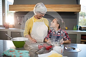 Smiling grandmother and granddaughter looking at each other while holding a bowl of flour