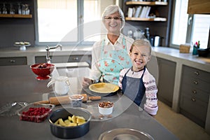 Smiling grandmother and granddaughter posing while making pie