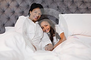 Smiling grandmother and granddaughter relaxing on bed at home