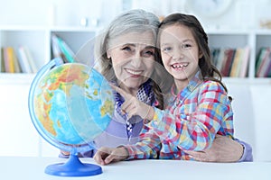 Smiling grandmother and granddaughter sitting at table with globe