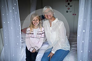 Smiling grandmother and granddaughter sitting together on bed