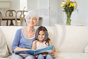 Smiling grandmother and granddaughter sitting together on sofa with photo album