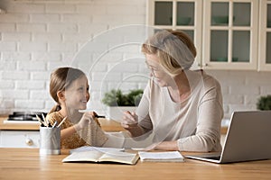 Smiling grandmother help granddaughter with homework assignment