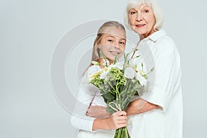 smiling grandmother hugging granddaughter with bouquet