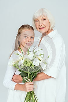 smiling grandmother hugging granddaughter with bouquet