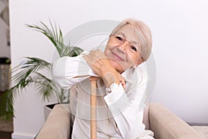 Smiling grandmother sitting on couch. Portrait of a beautiful smiling senior woman with walking cane on light background at home.